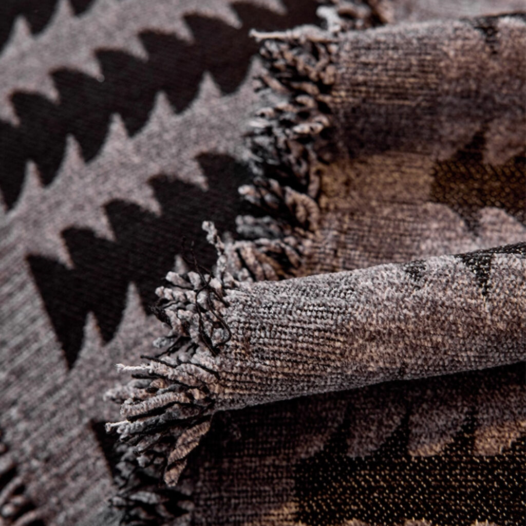 Gros plan sur la chenille tissée du plaid de canapé, motif forêt abstrait et franges