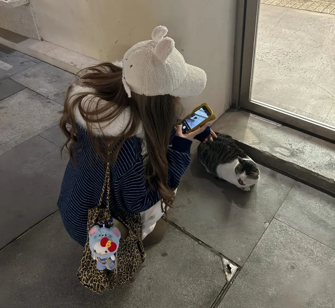Jeune femme accroupie à hauteur de son chat, smartphone en main, en train de le photographier — bonne technique de prise de vue pour photo d'animal