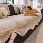 Chat roux sur un jeté de canapé kaki, main soulevant la bordure ondulée