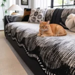 Chat roux allongé sur un jeté de canapé en chenille noir et blanc