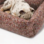 Chien qui dort en boule dans un panier en tweed rouge marron